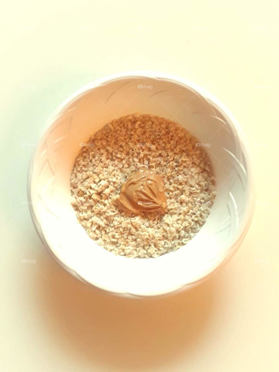 A minimalistic photo of a bowl of oatmeal with a scoop of peanut butter in a white bowl.
