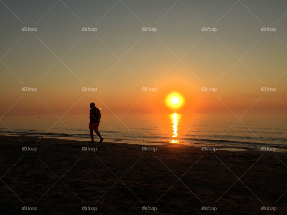 Man walking alone on the beach in the sunrise