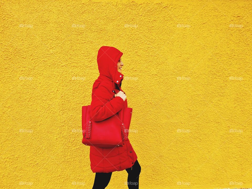 Profile woman with red hood walks in front of a yellow wall