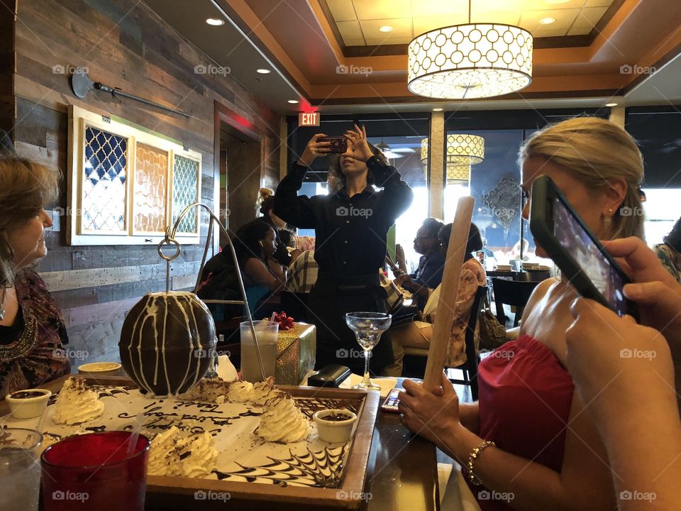 Waitress takes a group photo with chocolate piñata at restaurant with warm light ambiance and colors of red and black