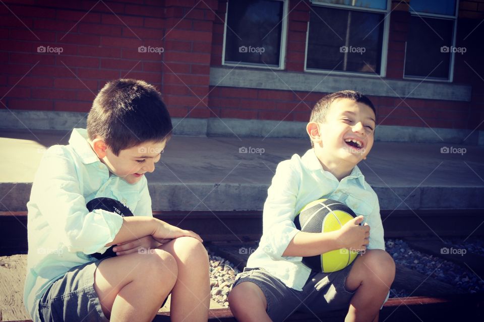 Brothers laughing and sharing special time sitting on a train track during the summer time 