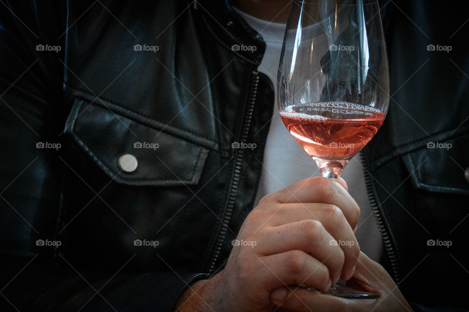 Man in a black leather jacket holding a wine glass with Rose in it.