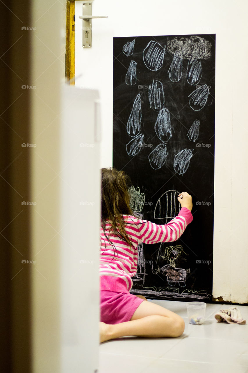 Creative at home - I put up a black board for drawing on the kitchen door for them to have fun with and be creative. Image of girl drawing with chalk.