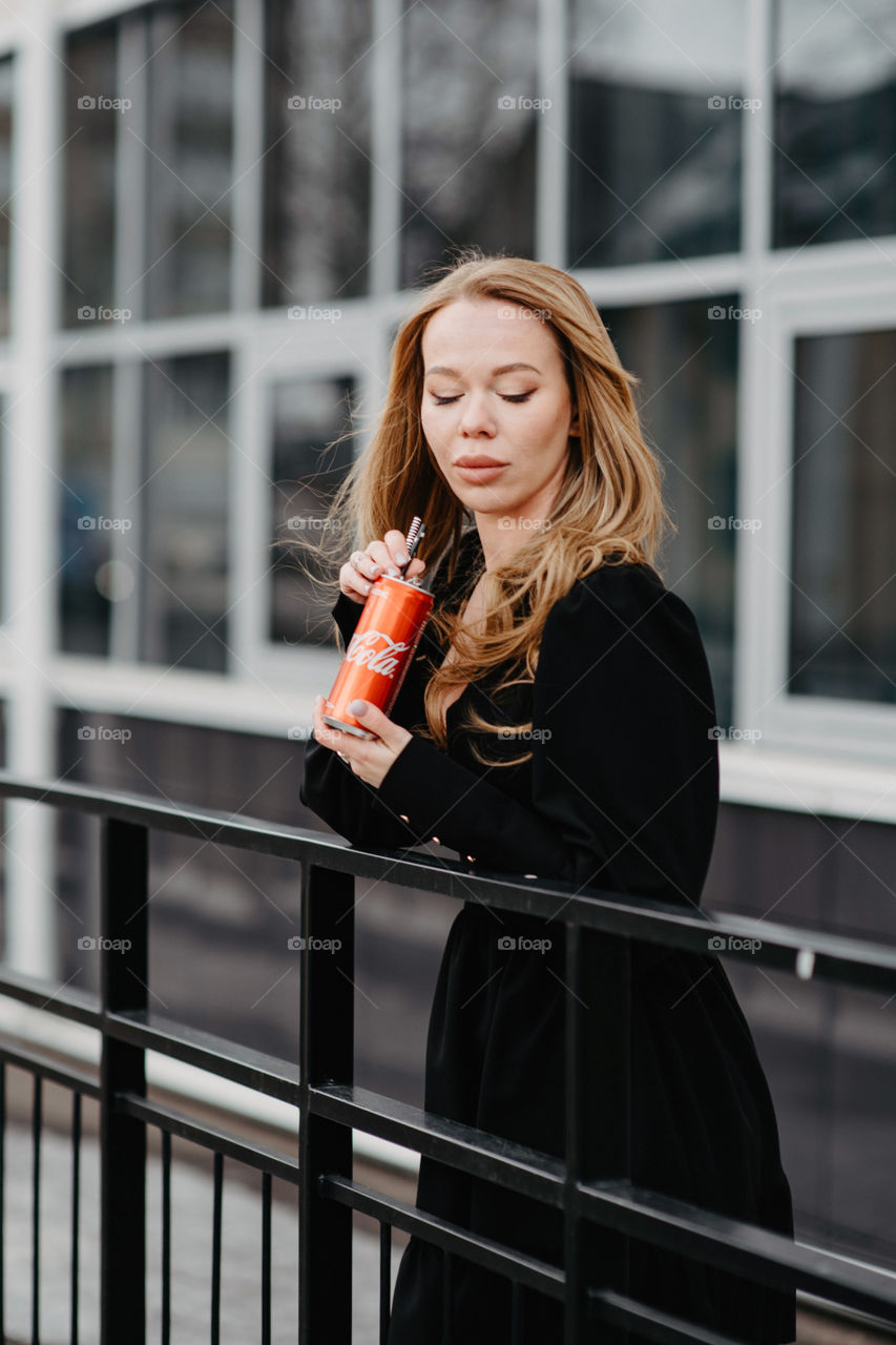 A woman in black dress drinks Coca-Cola. Holds red can in hands