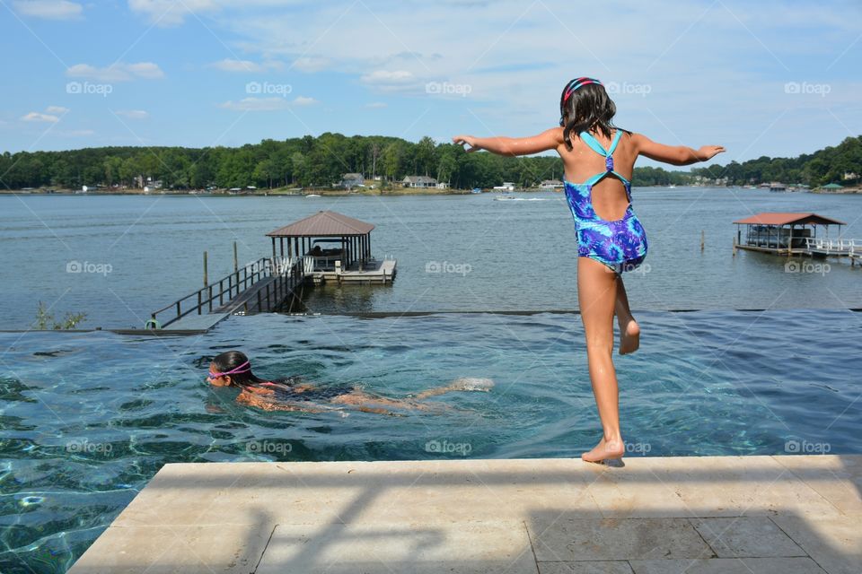 Girls jumping and swimming in infinity pool with lake in background