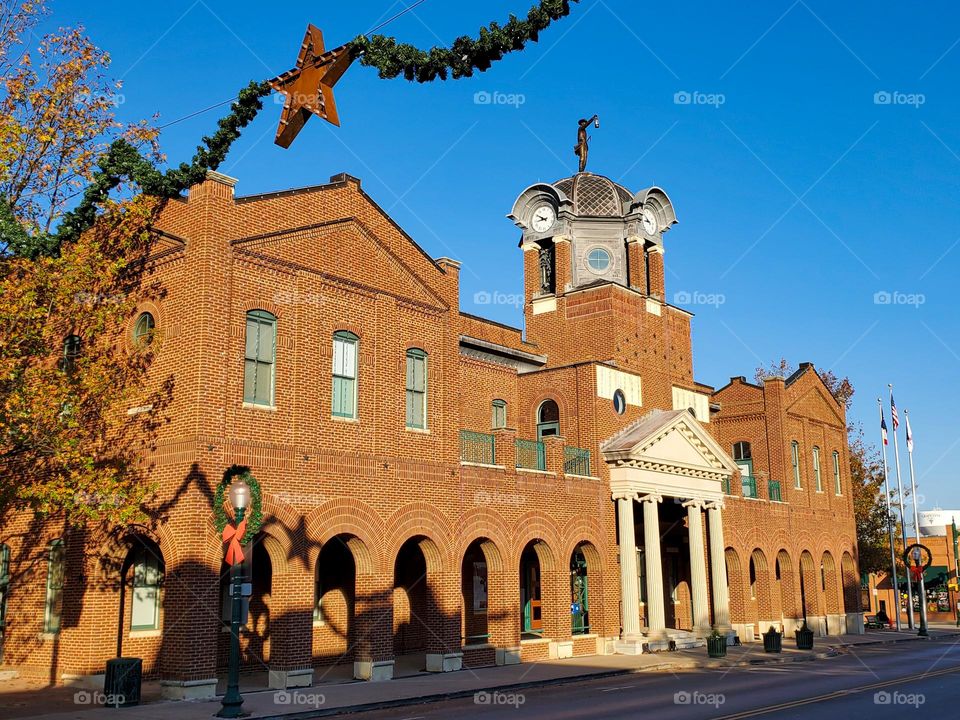 A beautiful brick building with a magnificent statue is framed by a Christmas decoration