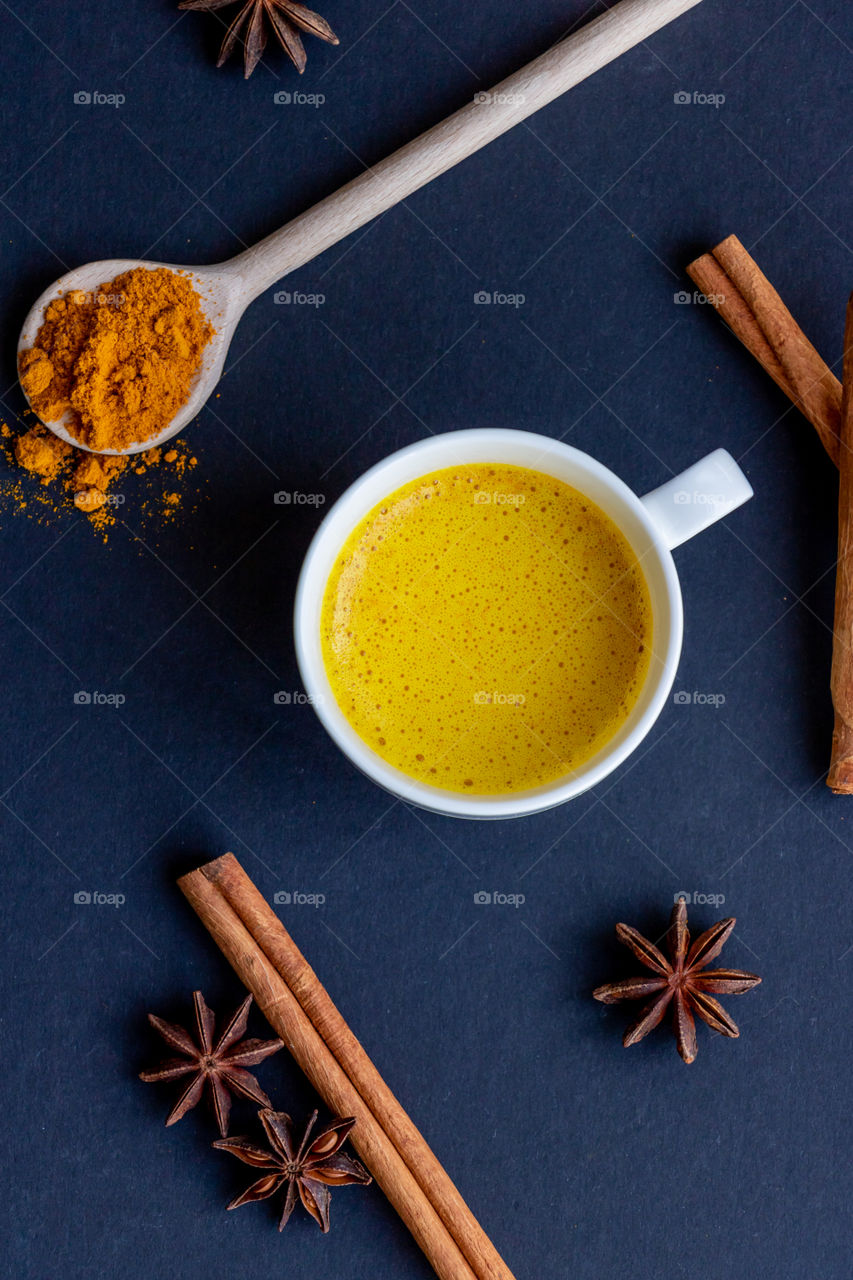 Top view to a cup with golden milk and some spices like cinnamon, anise and turmeric.