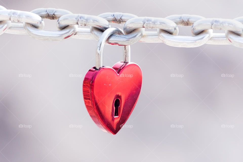 Red heart shaped metal padlock hanging on a shiny steel chain 