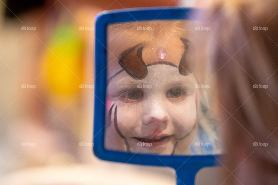 Child admiring her new reflection in a mirror after fun with face painting 
