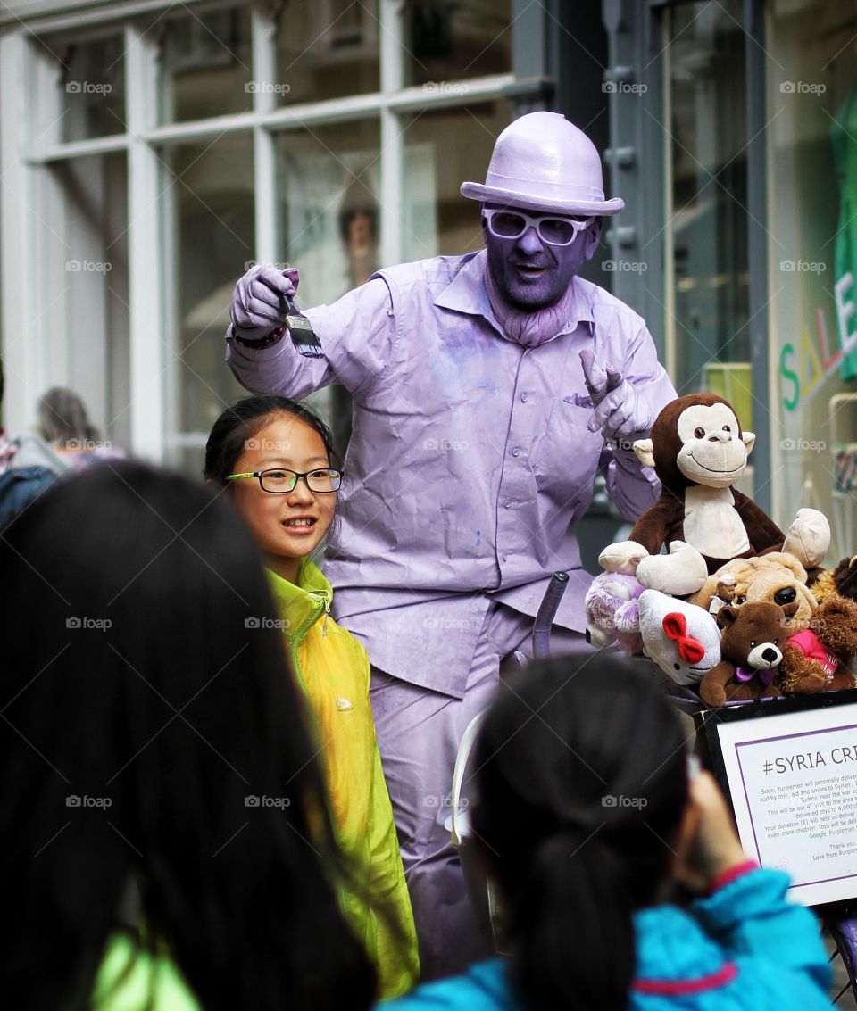 A street artist known as The purple Man painting Japanese tourists on the city streets of York.