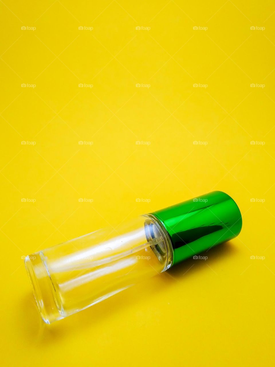 Transparent glass bottle of perfume product packaging with green bottle cap photographed in studio on yellow background.
