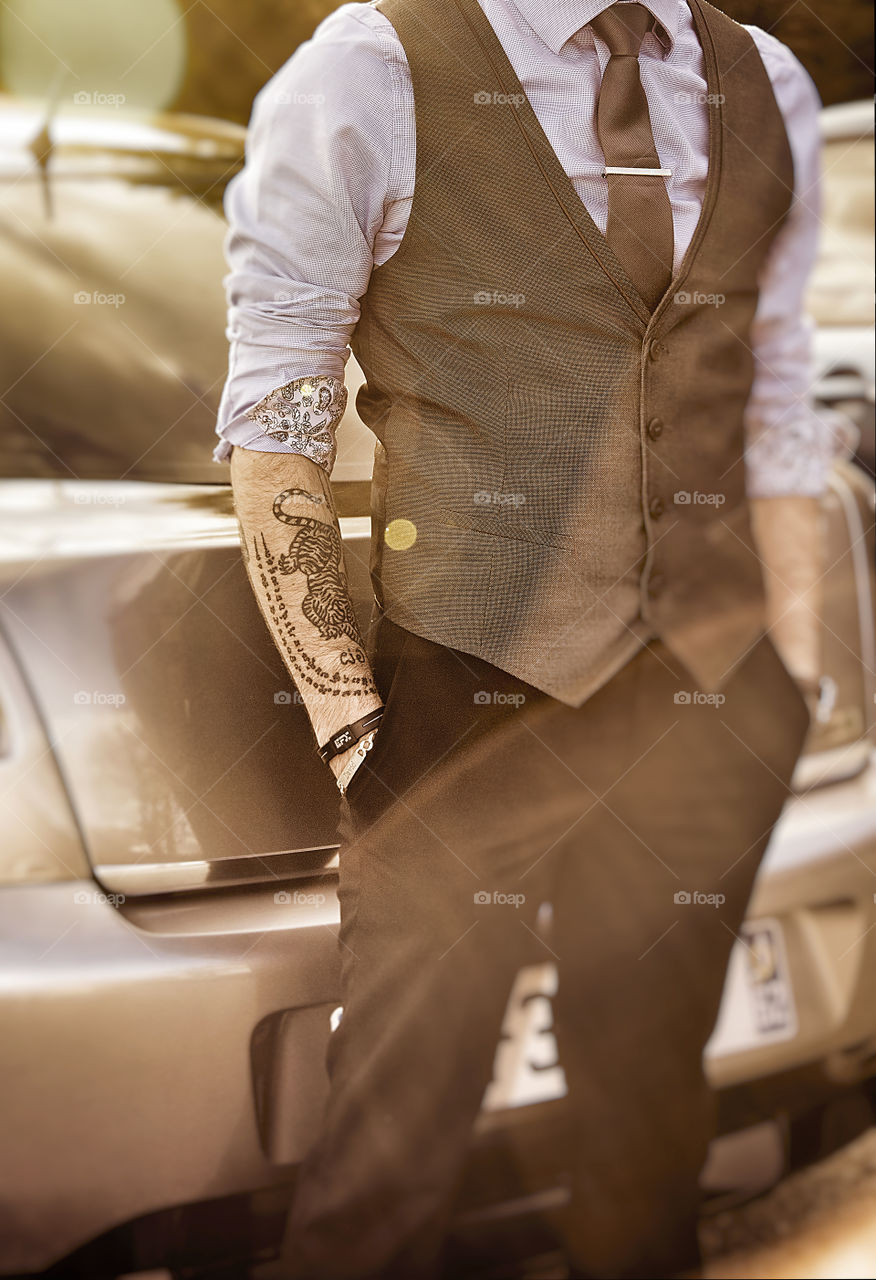 Portrait of a young man with tattoo on arm wearing smart casual business clothing standing next to a sport car