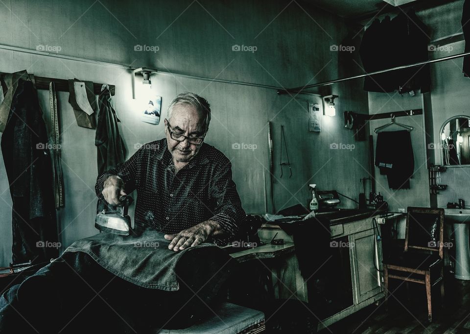 Senior man ironing cloths in shop