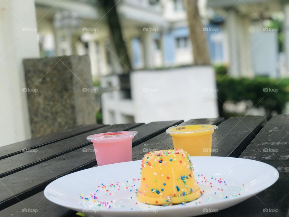 There is a yellow mango pudding in white plate over outdoor wooden table 