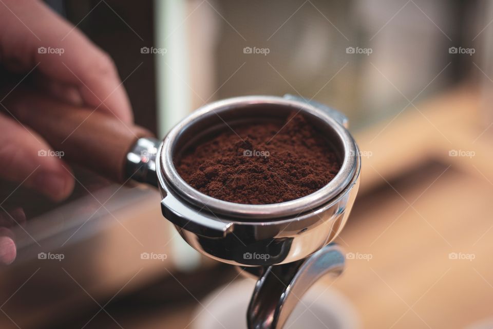 A close up portrait of freshly grounded coffee beans in a portafilter being held by a barista. ready to make a hot cup of coffee.