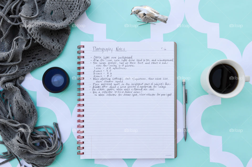 At-a-Glance notebook laid out open on a teal patterned backdrop with a pencil, camera lens, cup of coffee, grey blanket and silver decorative bird