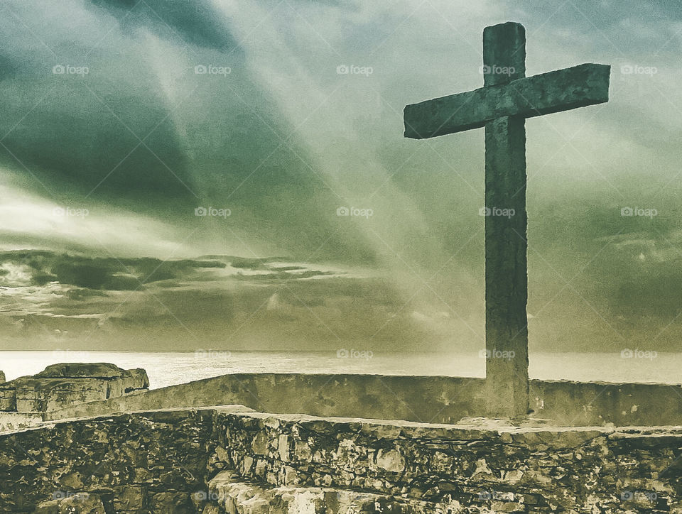 Stone cross captured in a glimmer of sunlight on a stormy day at Peniche on the Atlantic coast of Portugal