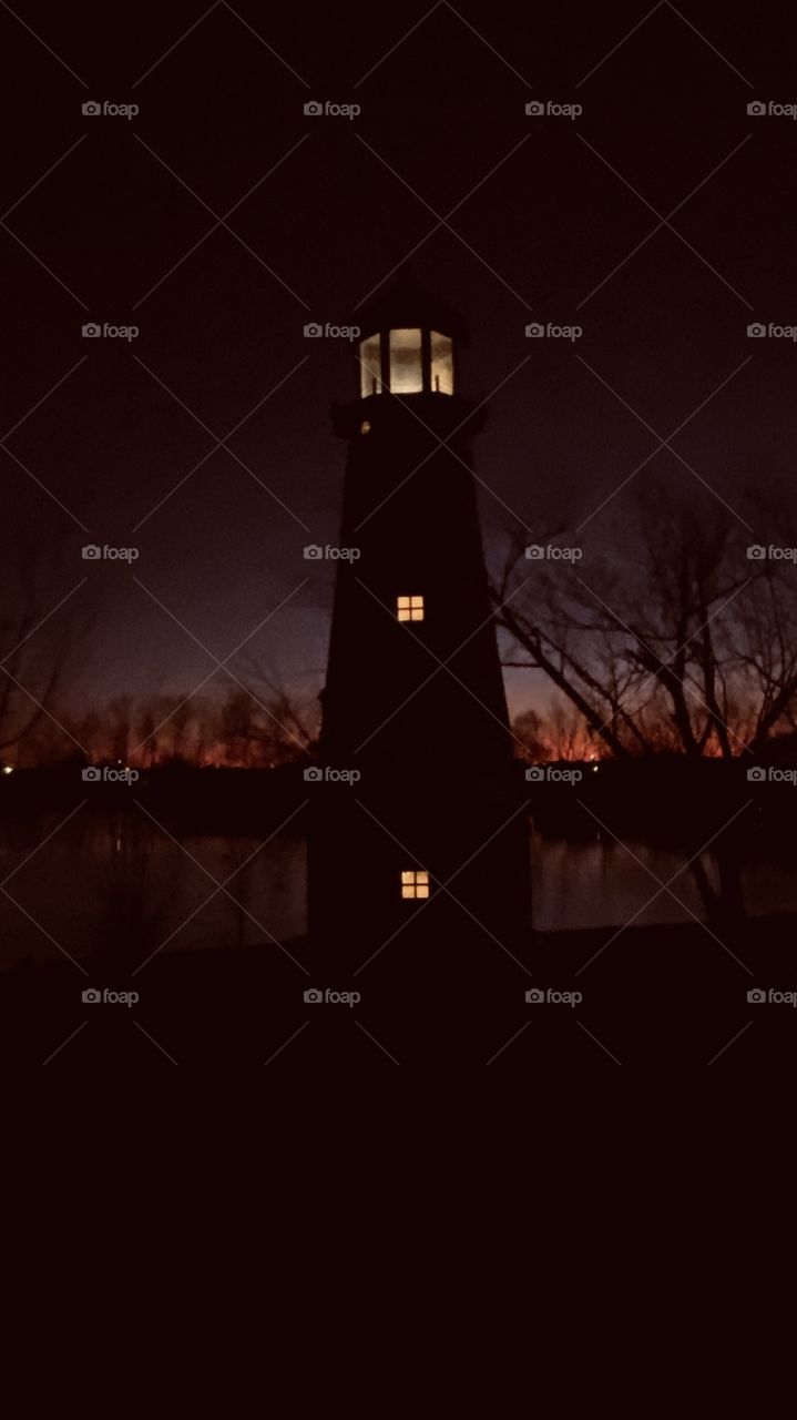 Sunset-Twilight-Night Lighthouse shining. Blends in with Back Light Features and nice Colors. Also BackLit to Horizon with Reflections of Shoreline on Lake Waters.