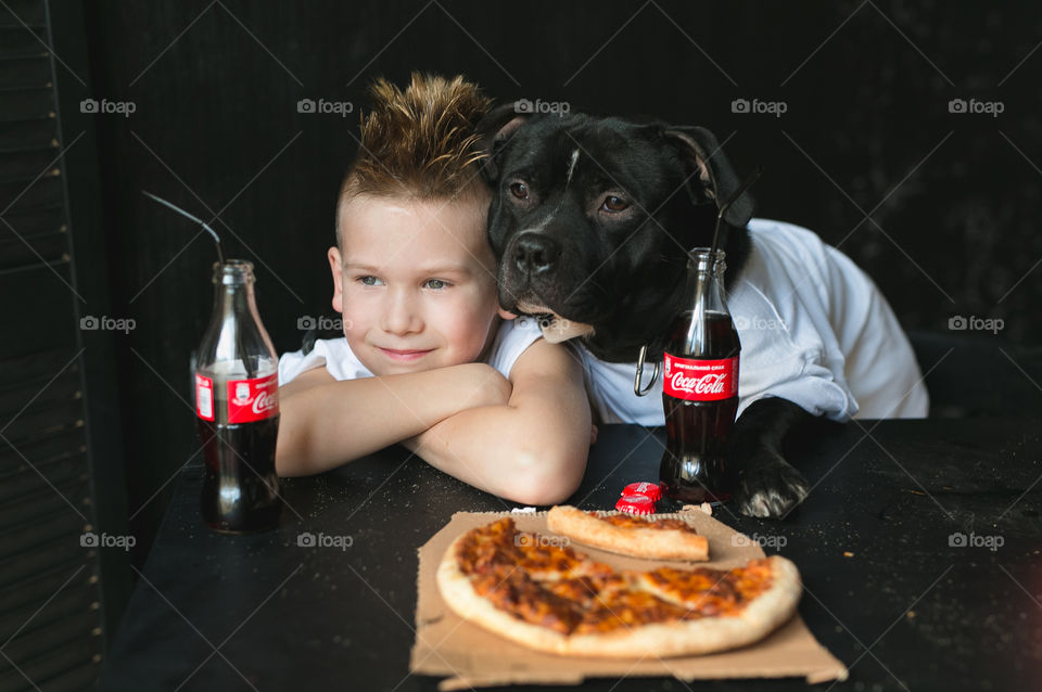 cute boy in a white T-shirt with his dog in a white T-shirt, sitting at the table, eating, drinking Coca-Cola, looking out the window