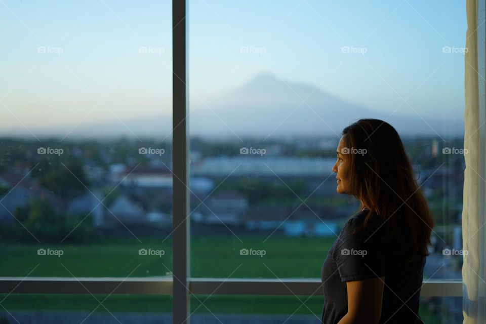 asian woman standing behind window with beautiful mountain view