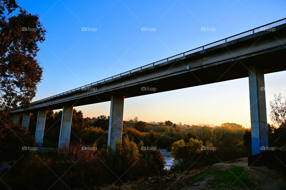 The beautiful sunset reflecting on the bridge side and trees and water.