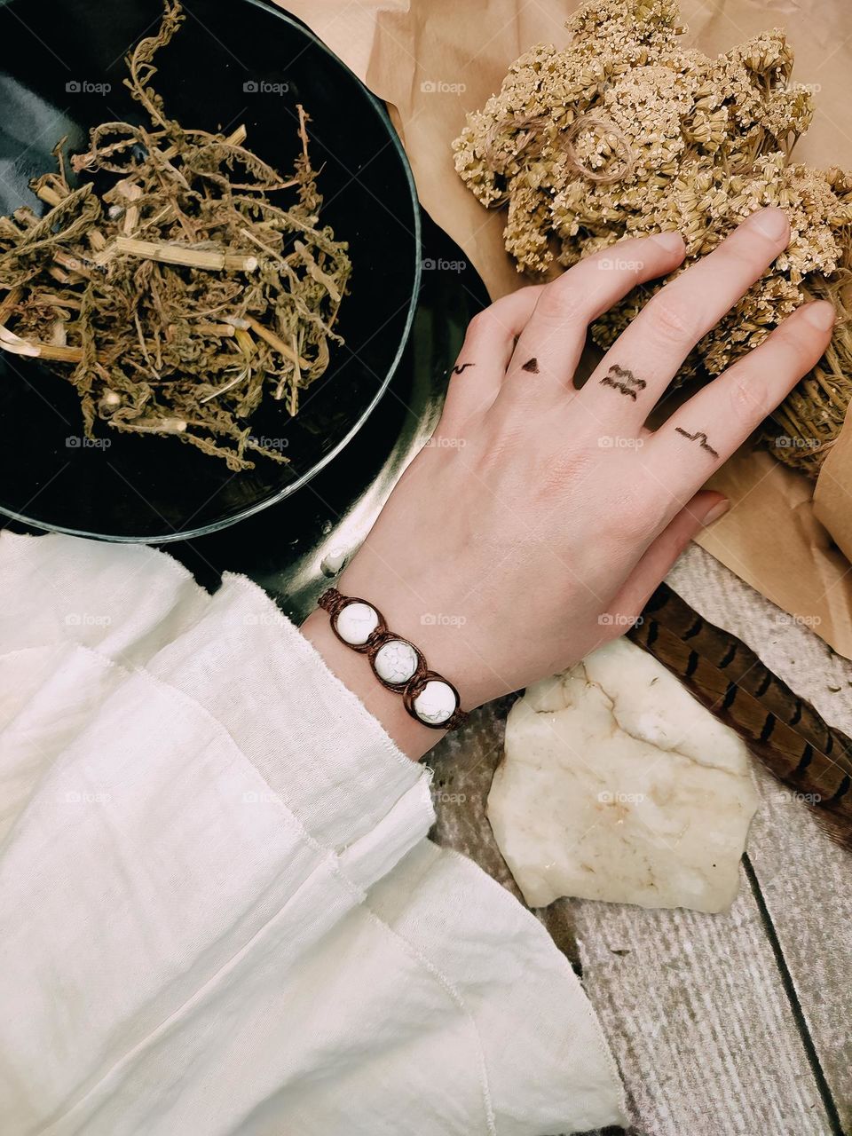 Meditation with herbs, minerals and aromatic sticks. Woman's hand in white stone bracelet, magical symbols on fingers