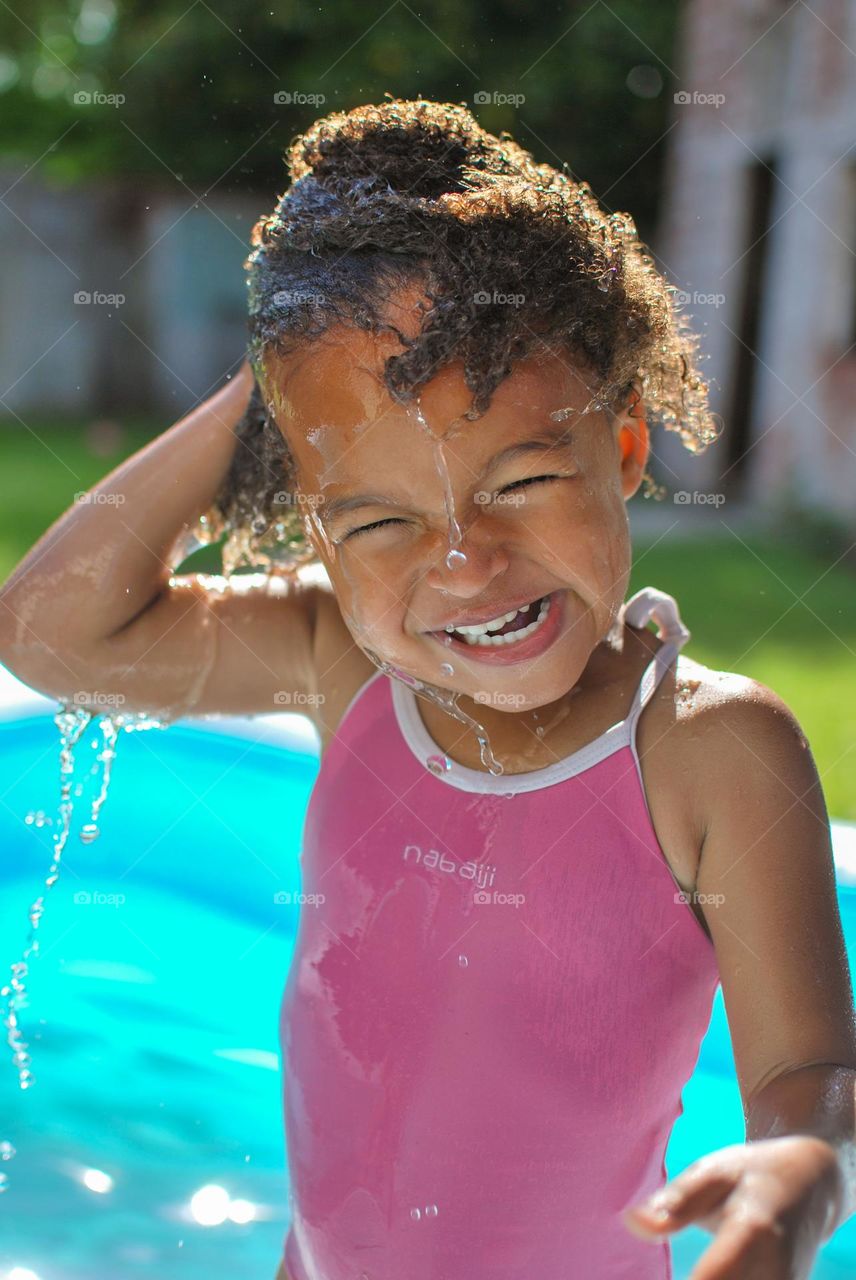 Girl of mixed race enjoying the refreshment of water in a swimming pool on a hot summer day (family, fun, summer, water, blue, swimming suit, splash, hot, enjoy, play, outdoors
