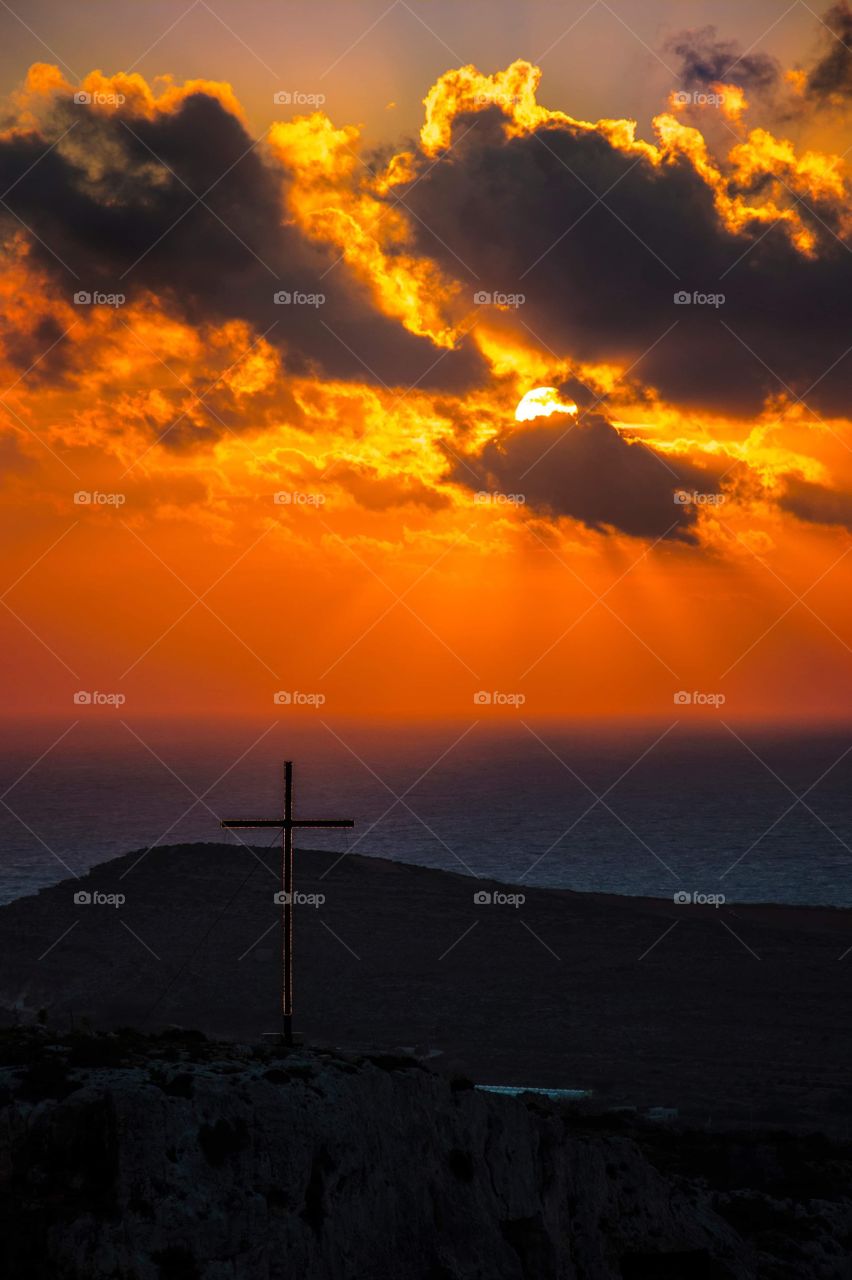 Sunset over the Mediterranean Sea, with a lit up cross in the foreground. Photograph was taken in Mellieha, a village in Malta.