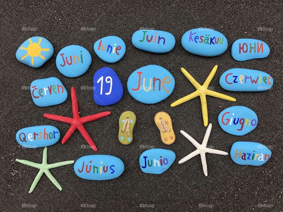 19 June, calendar date with multicolored stones and starfishes over black volcanic sand