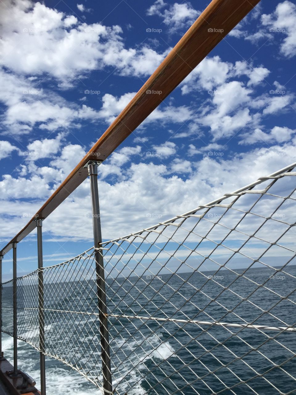 Safety net on boat. Blue ocean and sky dotted with clouds from boat