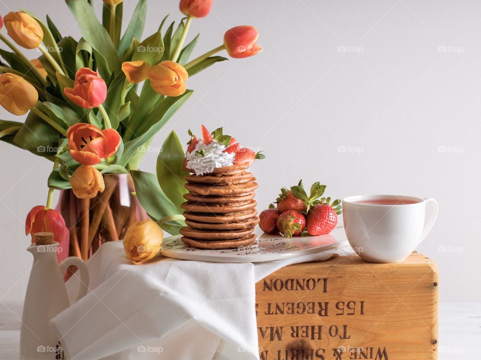 Pancakes served with whipped cream and strawberries, cup of tea and beautiful spring flowers