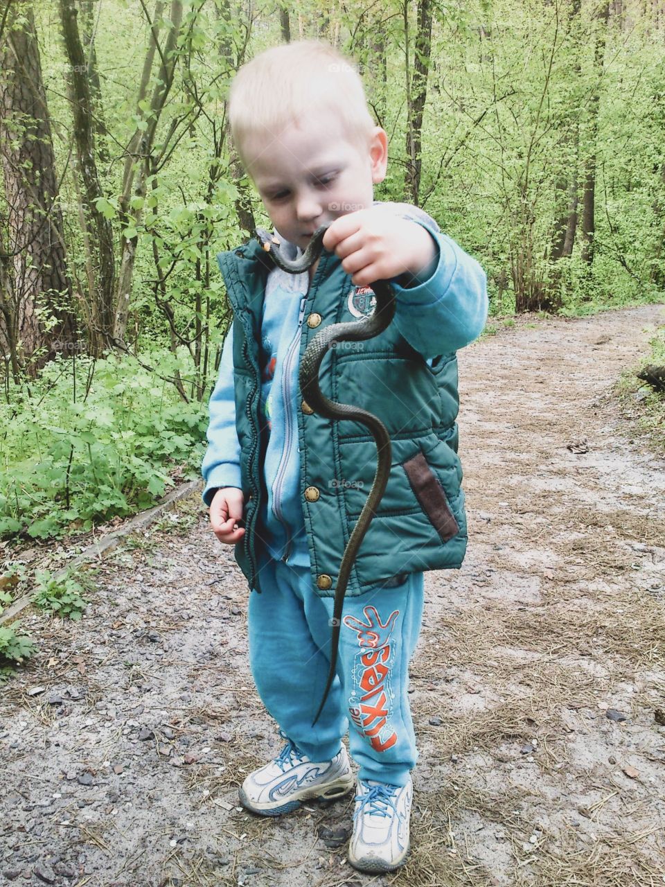 little boy holding a snake in the forest