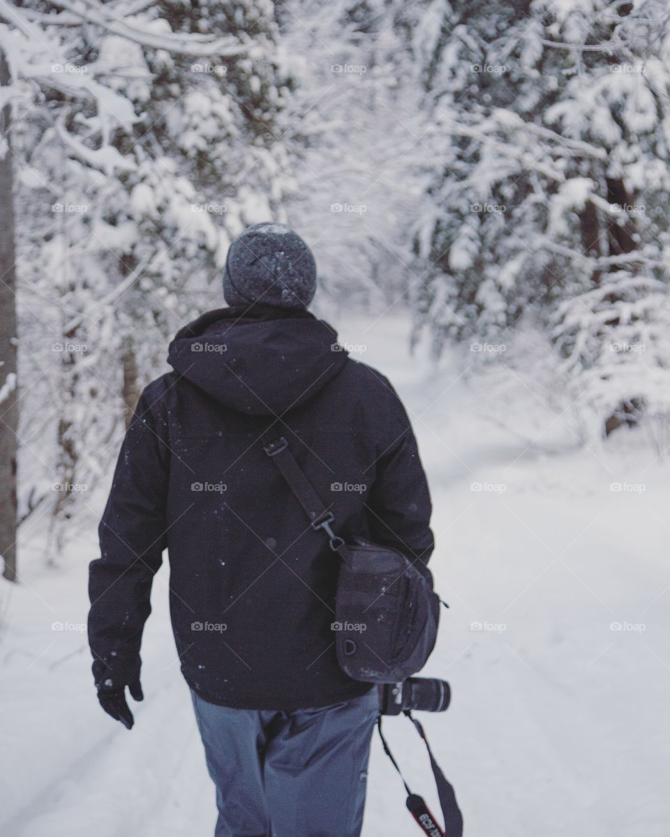 A young man walking through a snowy forest with his camera, exploring