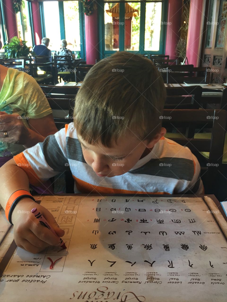 While waiting for the food, the boy is learning chinese writing. He is very concentrated on the task. He's learning.