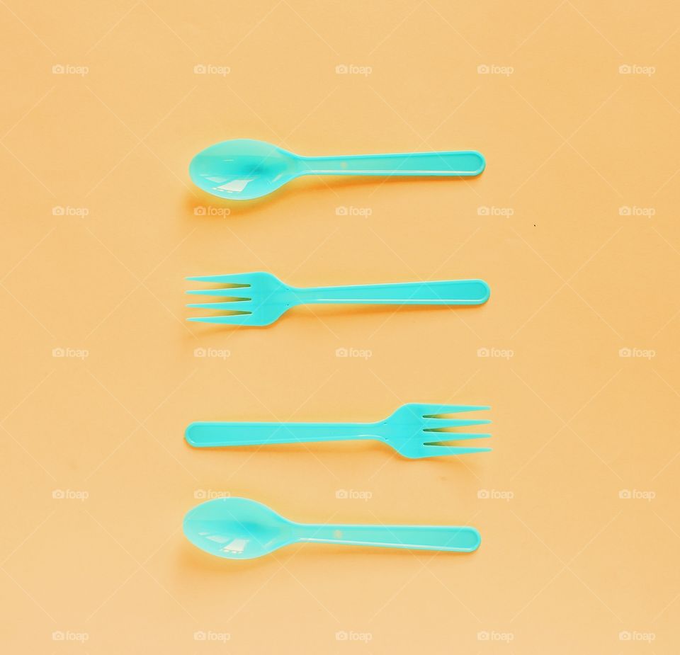 Plastic spoons and forks on orange background