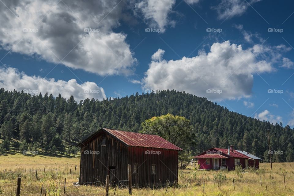 A barn with a red roof in a valley surrounded by trees on hills
