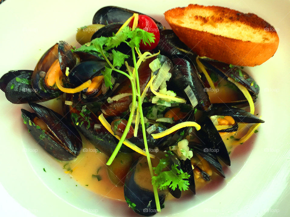 Closeup of a plate of steamed mussel in a lemongrass curry sauce. Topped with parsley, a bright cherry tomato and perfectly toasted garlic bread to soak up the delicious sauce. Yummy!