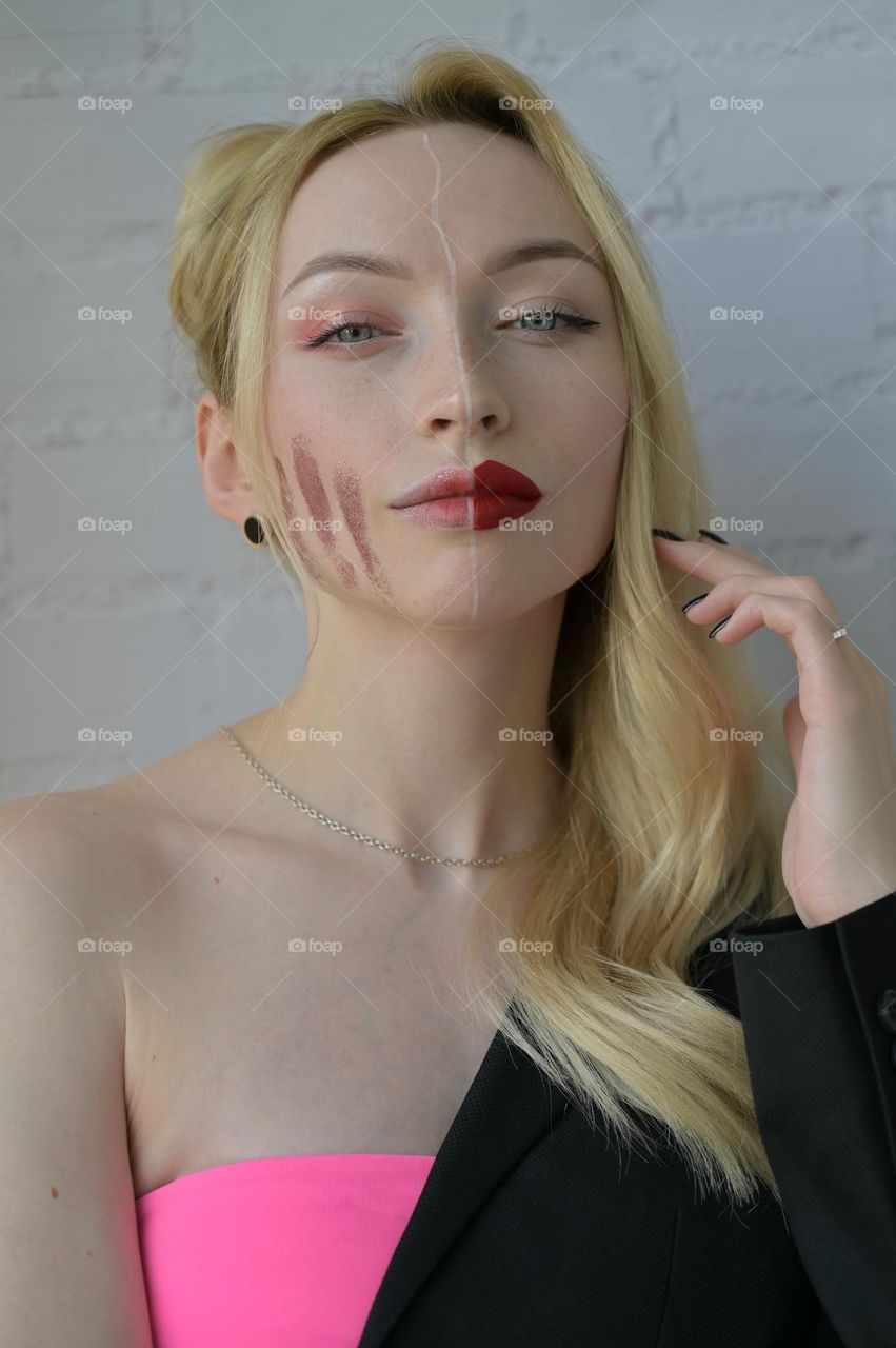 Close-up portrait of a blonde girl with different make-up on half of her face with her hand near her hair on white background