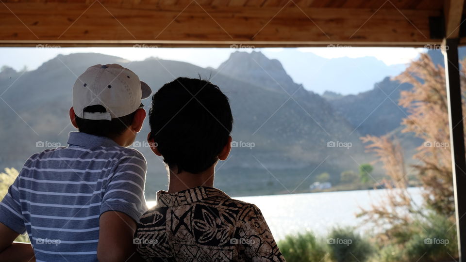 Father and son sitting by a lake, admiring the landscape.