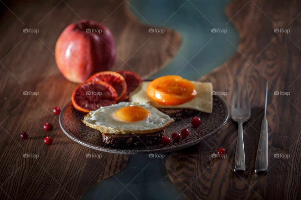 Grain bread with egg, tomato, cheese and bacon on ceramic plate with red orange to desert