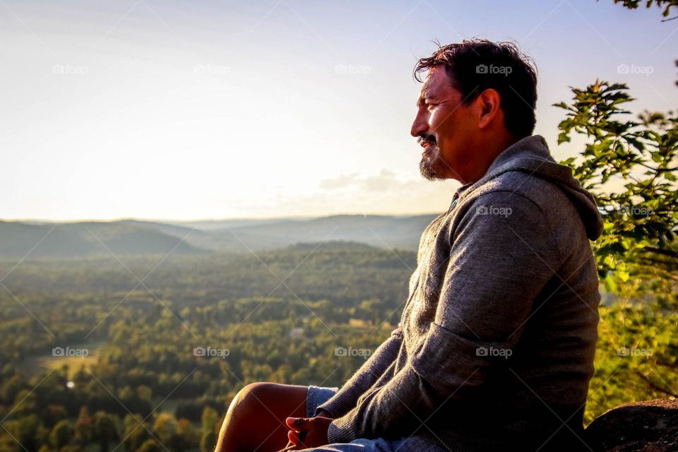 Man with a beard is looking at a beautiful landscape sitting on a rock