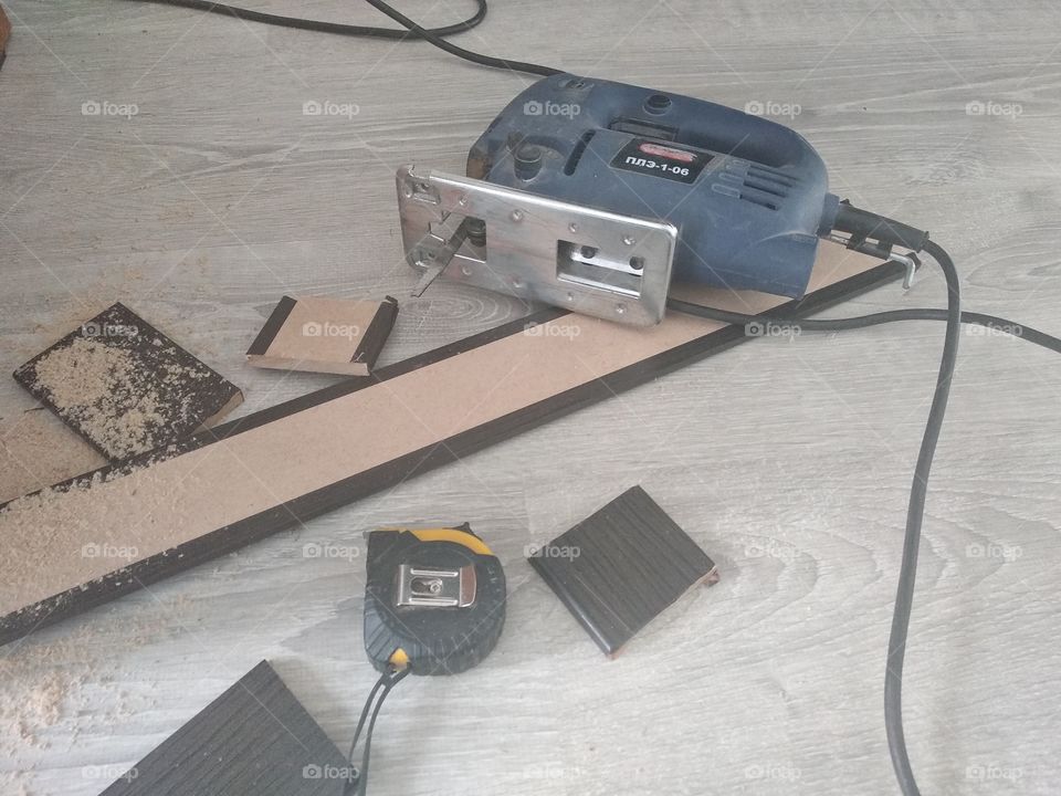 Construction tools (electric jigsaw and measuring roulette) on boards in sawdust on a light wooden floor