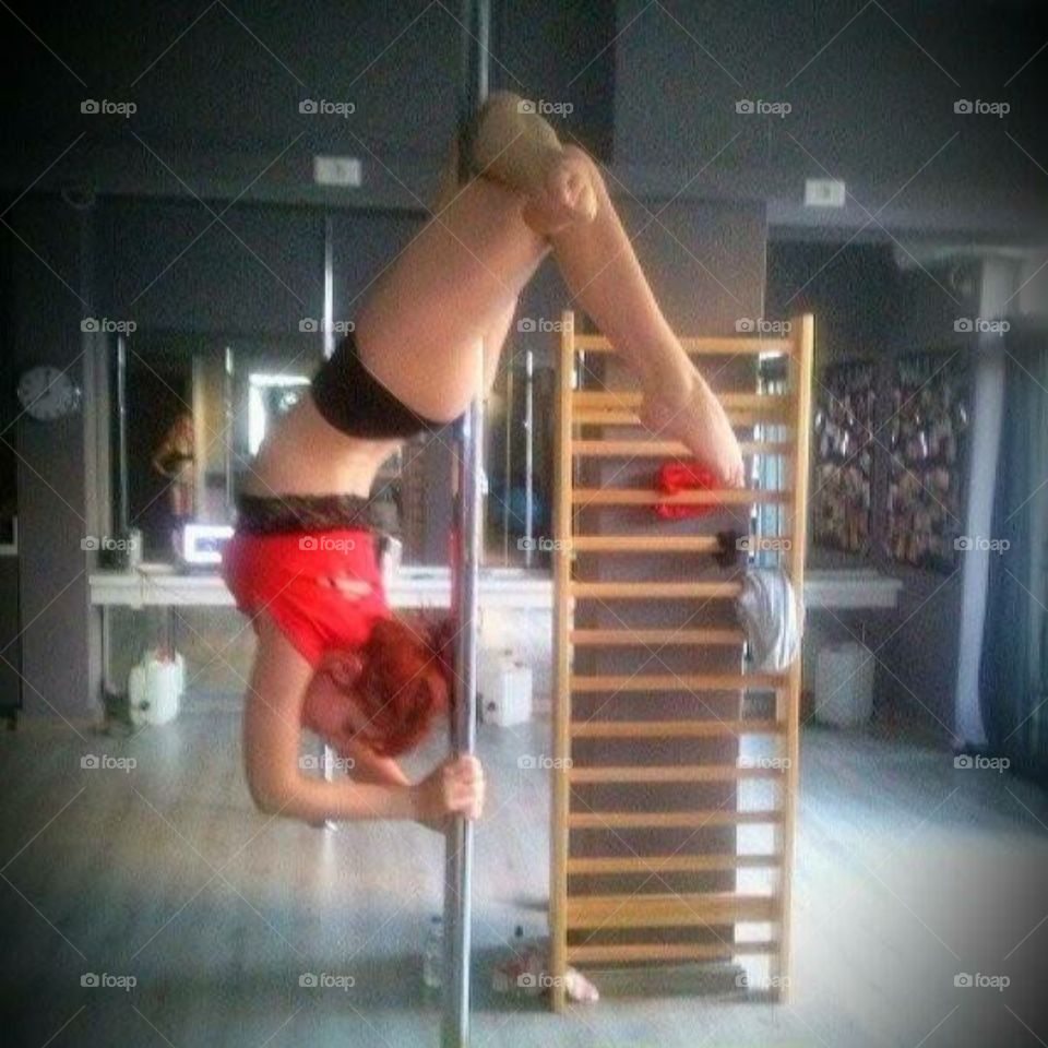 A young woman dancer posing upside down on pole