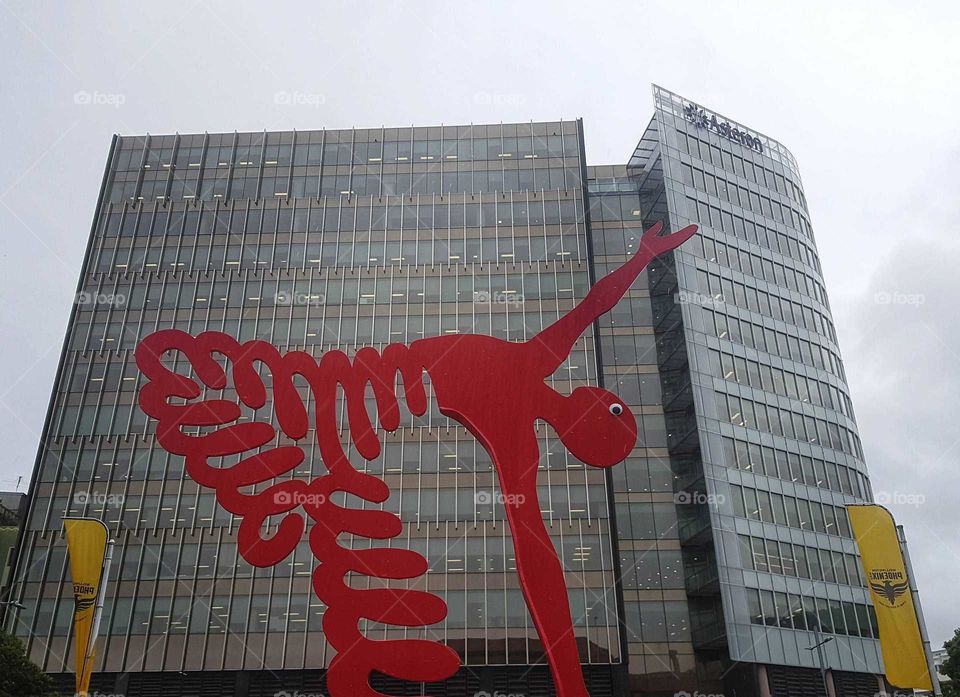 An art sculpture in red reaches for the sky in front of a big tall building in Wellington city. NZ.