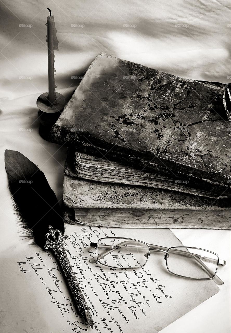 Writer's morning. Old books, a piece of paper with handwritten text, glasses, a ink pen and an extinguished candle. Black and white photo