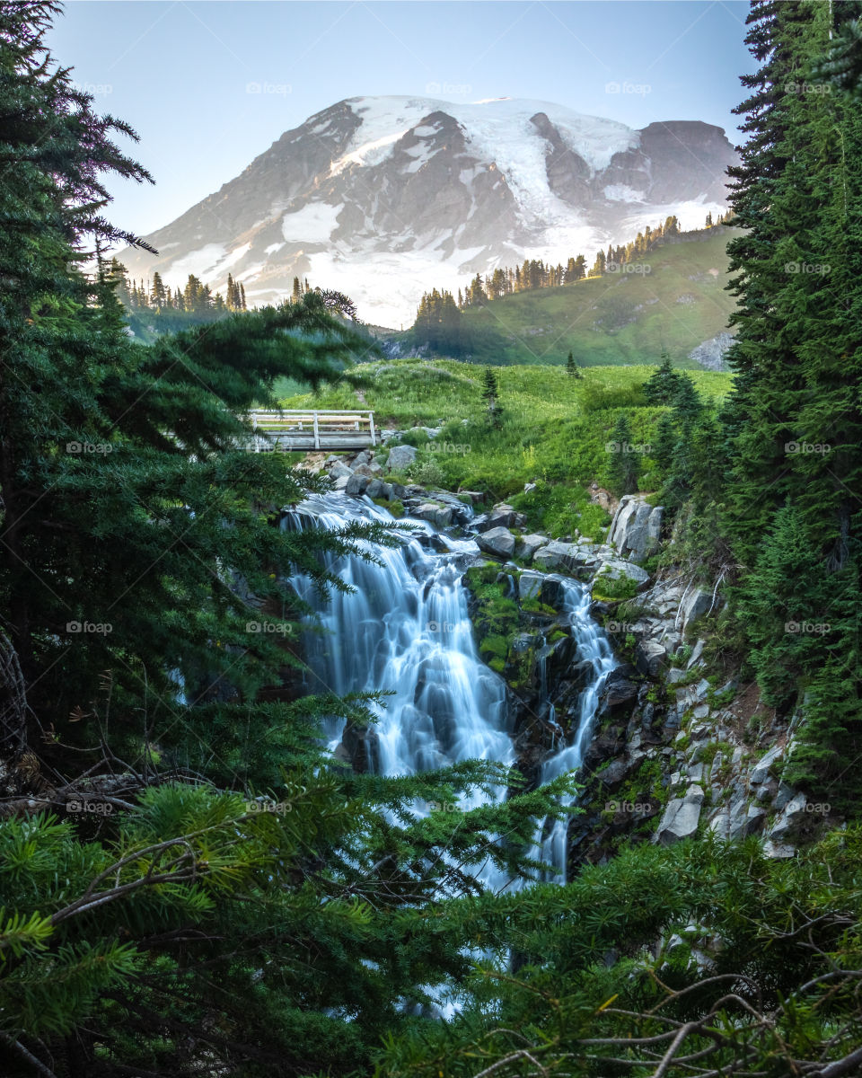 Crystal clear water cascading down a waterfall in the mountains, as snow capped peaks remain in higher elevations. 