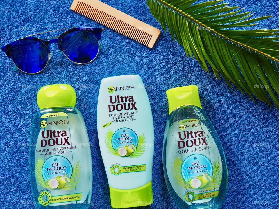 Garnier shampoo, conditioner and bath gel on a blue towel with comb and palm leaf and blue sunglasses.
