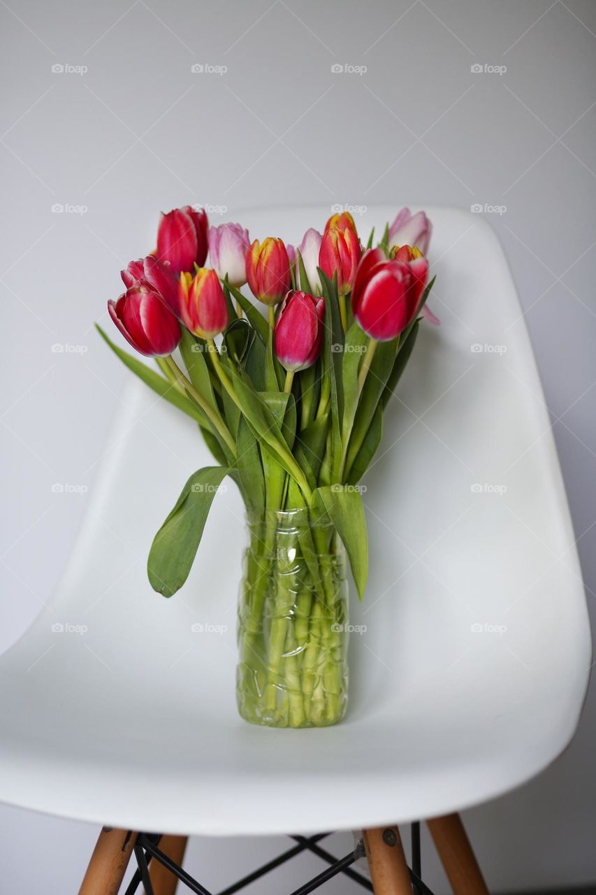 a transparent vase with tulips stands on a white chair