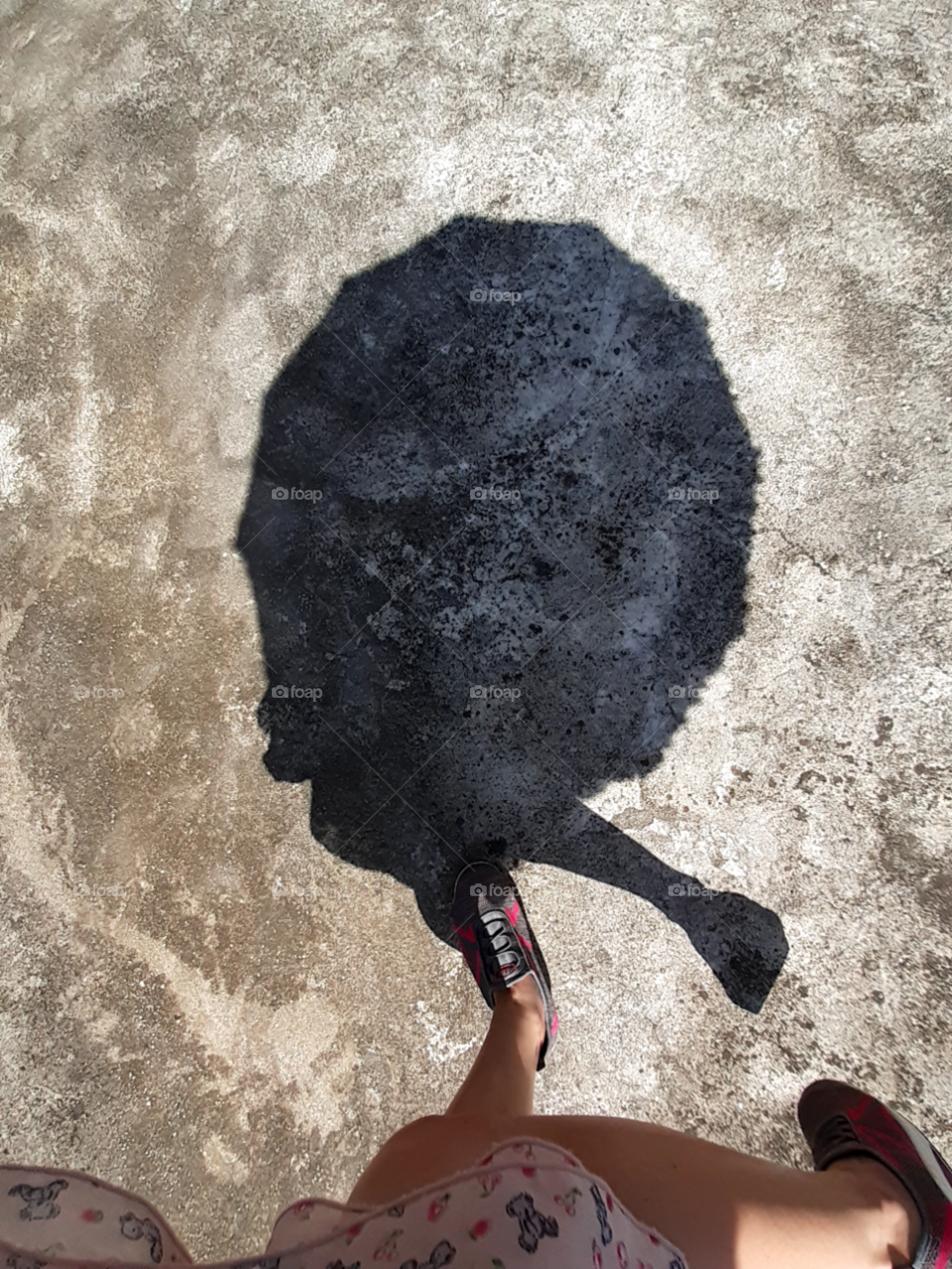 A shadow of an umbrella and the legs of the woman that carried it under the hit of the sun.