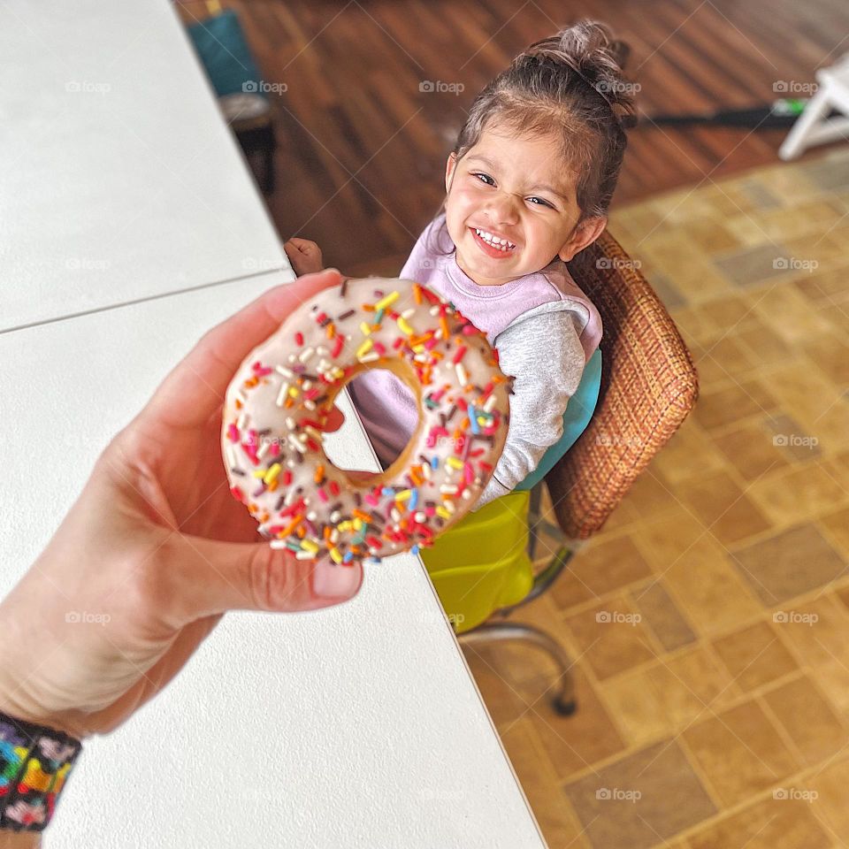 Handing a donut to a toddler girl, toddler girl is excited for a donut, circles in everyday life, circular shapes all around us, toddler girl loves donuts, toddler excited to eat a donut, donut with vanilla frosting and sprinkles